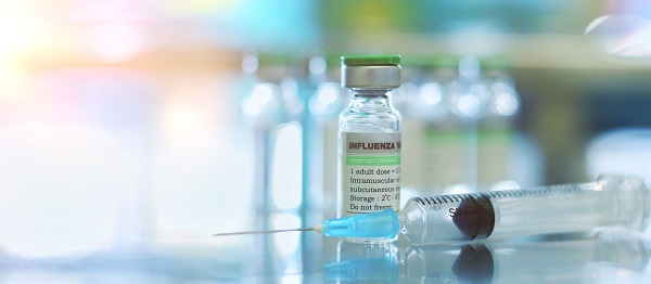 Vials of flu vaccine sit on a table with a syringe.
