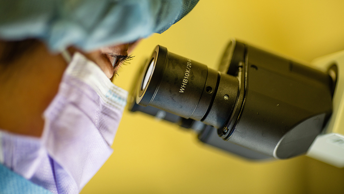 Doctor wearing a mask looking through a microscope